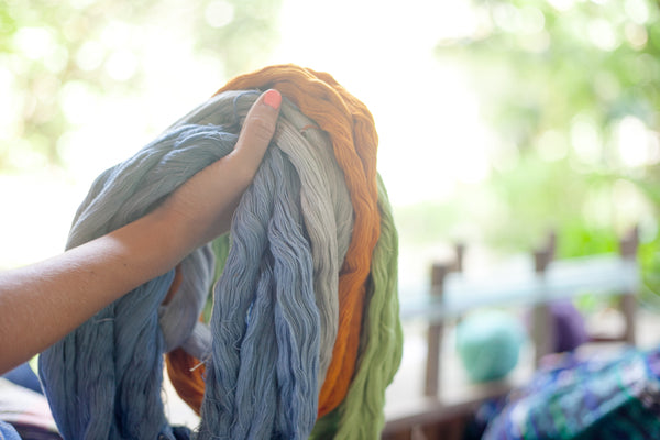 Model holds assorted bundles of dyed fabric in orange, blue, and grey strands, maya weaving workshops, how to see maya weavers work, handcrafted textiles from Guatemala