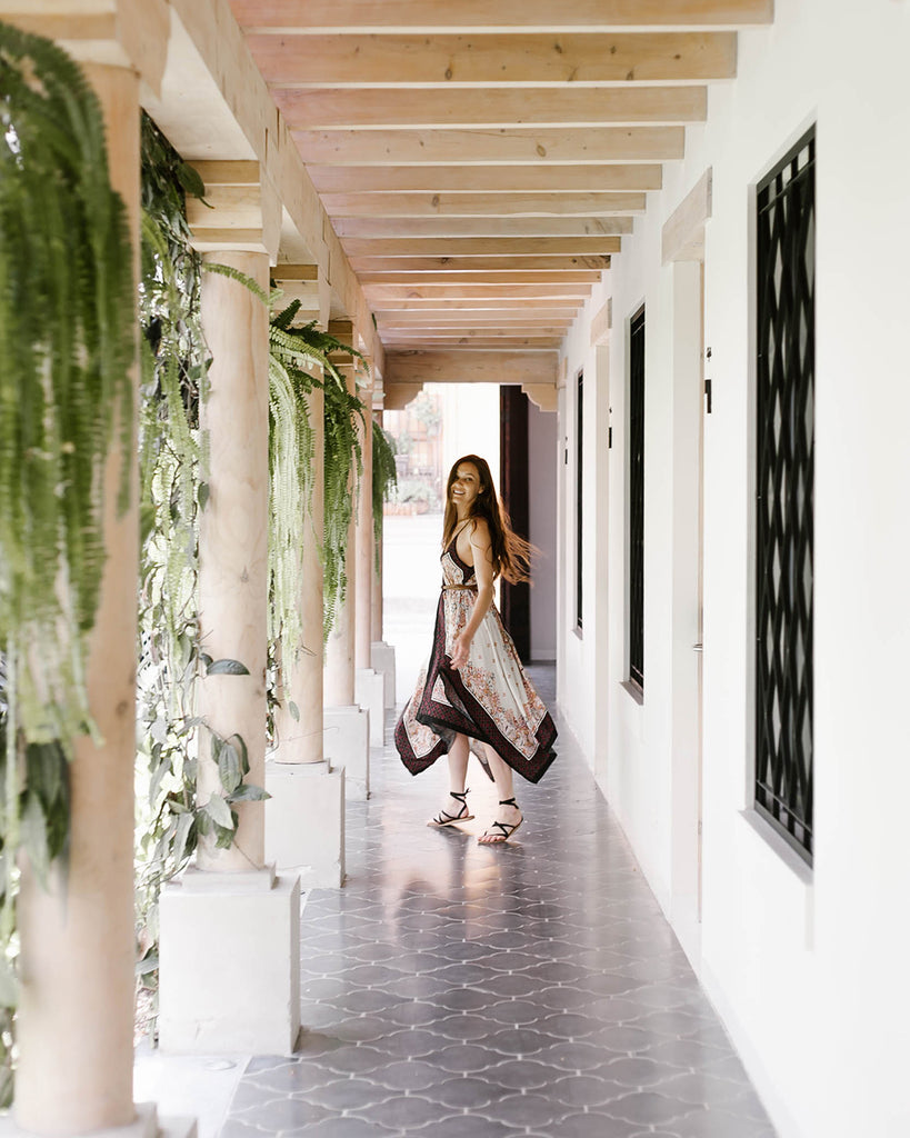 Light streams through pillars covered by plants as She Is Not Lost blogger Carina Otero poses in hallway at The Good Hotel, Antigua hotels, Antigua resorts, best places to stay in Antigua, ethical travel bloggers