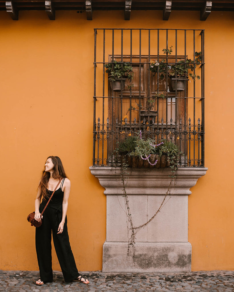She Is Not Lost blogger Carina Otero poses with Hiptipico leather crossbody bag in front of orange building with black iron window rods, ethical travel blogs, ethical travel in Antigua, what to do in Antigua, how to travel ethically in Guatemala
