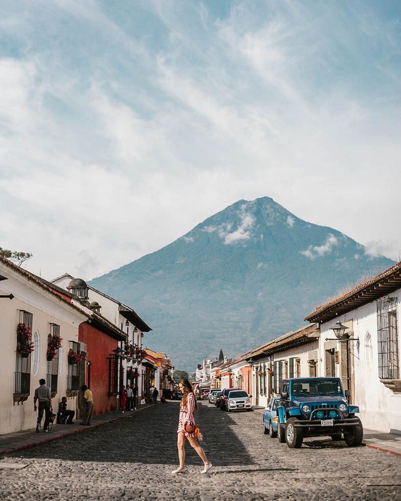She Is Not Lost blogger Carina Otero walks thoughtfully on brick road in Antigua Guatemala with volcano in the horizon, volcano travel destinations, tropical travel destinations, best central american travel locations, blogs about central america, guatemala travel blog, ethical travel companies