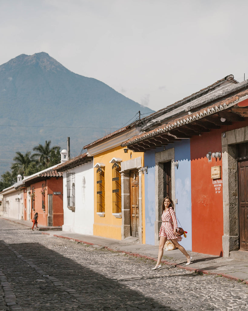 She Is Not Lost blogger Carina Otero steps onto paved brick road in front of yellow, blue and red colored buildings, ethical bloggers, travel blogs, travel blogs on Antigua, travel blogs about Central America, travel blogs Guatemala, ethical travel programs in Guatemala