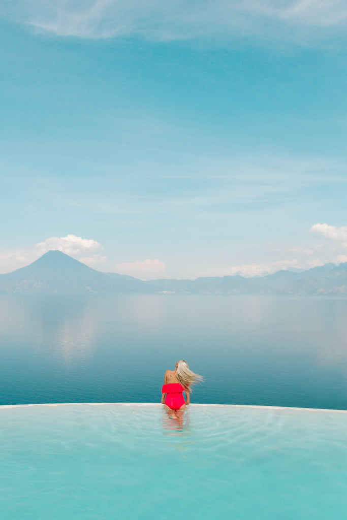 Hiptipico founder Alyssa looks over edge of infinity pool with light blue water in contrasting red suit overlooking Lake Atitlan, Lake Atitlan views, best views on Lake Atitlan, ethical travel bloggers, ethical travel blogs on Central America, where to travel in Central America