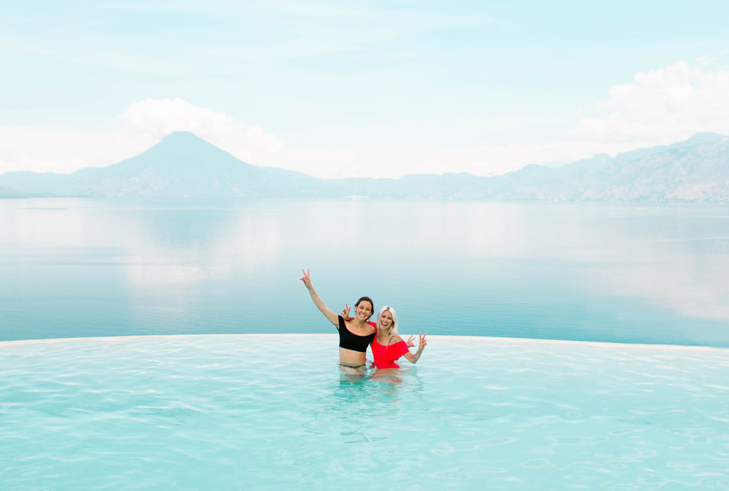 She Is Not Lost blogger Carina Otero and Hiptipico founder Alyssa Yamamoto pose with peace sign at Tzampoc resort pool overlooking Lake Atitlan, She Is Not Lost Travel, Travel Blogs, Ethical Travel Bloggers, Sustainable Travel, How To Travel Ethically, Guatemala Ethical Brands