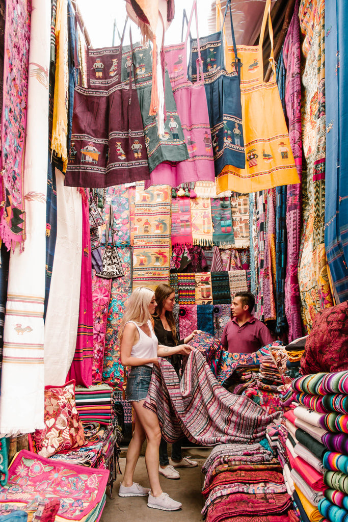 Hiptipico founder Alyssa and She Is Not Lost blogger Carina work with artisan to source textiles in colorful Chichicastenango market stall, ethically sourced textiles, ethical fashion in Guatemala, sourcing ethically in Guatemala