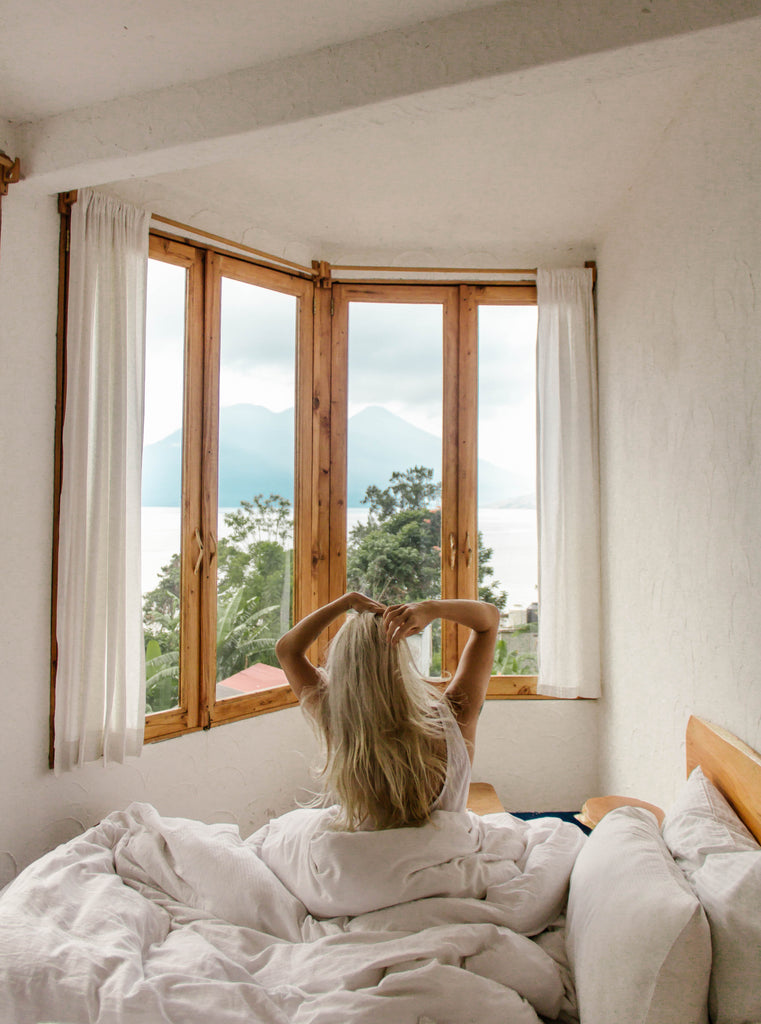 Hiptipico founder Alyssa looks out window in her room at Lush Atitlan ecohotel from bed with fluffy white sheets and pillows, ecohotels in Guatemala, ecofriendly lodging in Guatemala, ecofriendly resorts in Lake Atitlan, where to stay in San Marcos, San Marcos hotels
