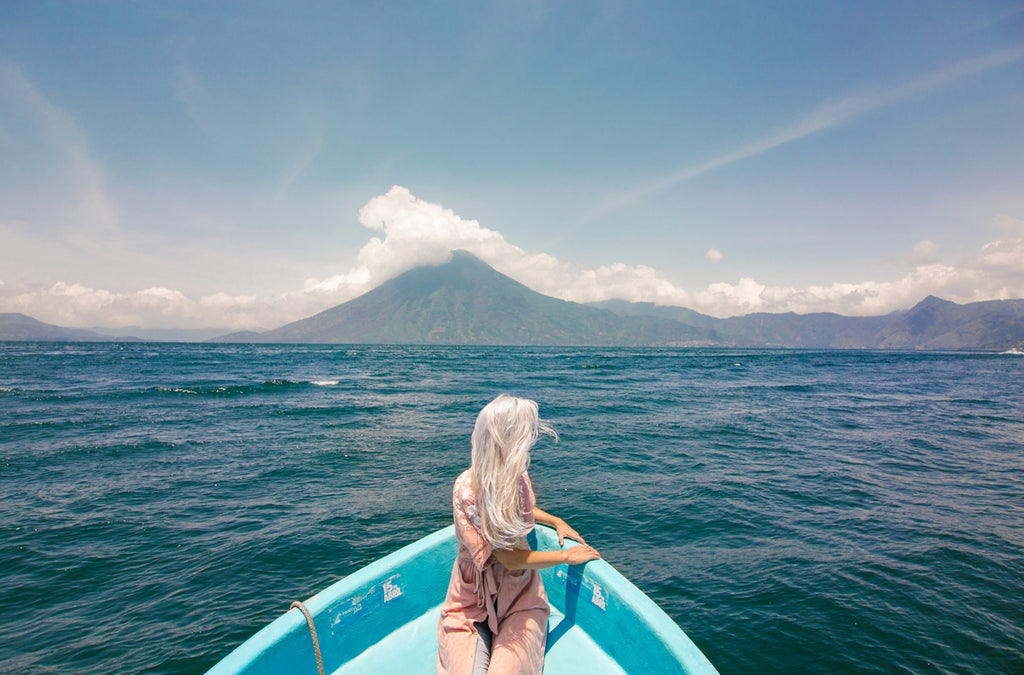Hiptipico founder Alyssa looks over the helm of a blue boat on vast Lake Atitlan in flowy pink cardigan and light-washed jeans, ethical travel, lake atitlan destinations, where to go on Lake Atitlan, best swimming in lake atitlan