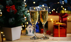 An image of two champagne glasses with a Christmas tree and presents in the background.