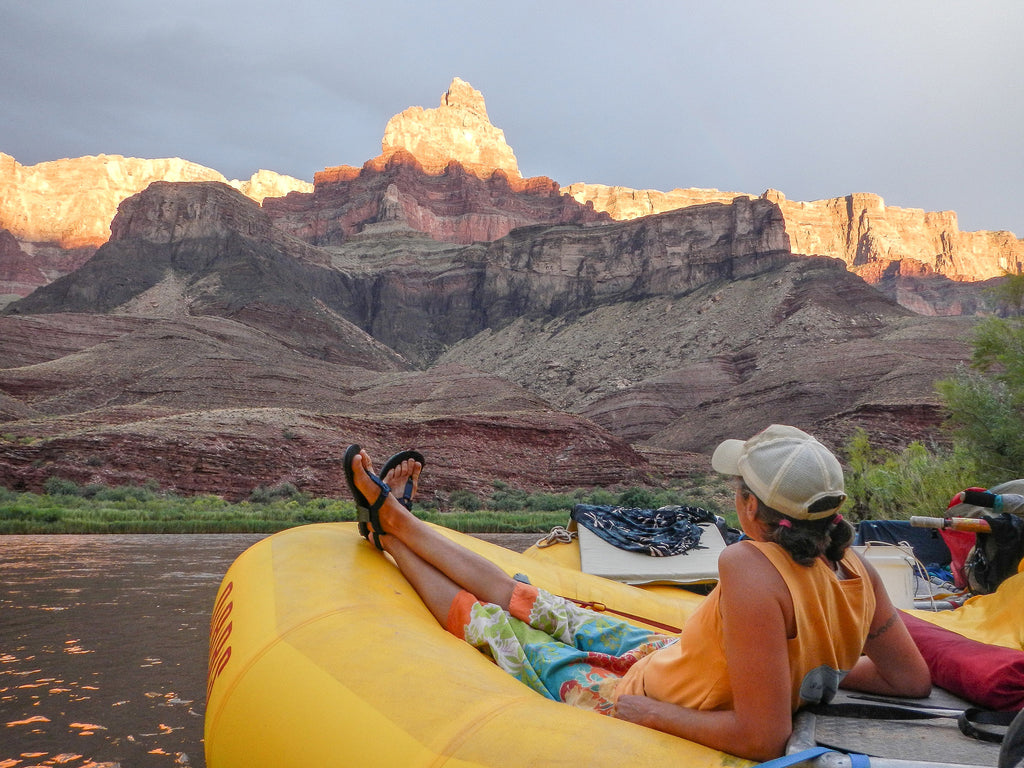 A whitewater guide lounging on their raft wearing trusty Bedrock adventure sandals