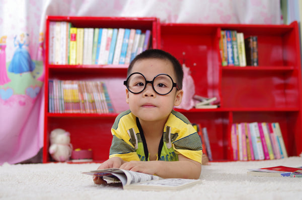 Boy in glasses laying on his tummy in front of a red bookcase