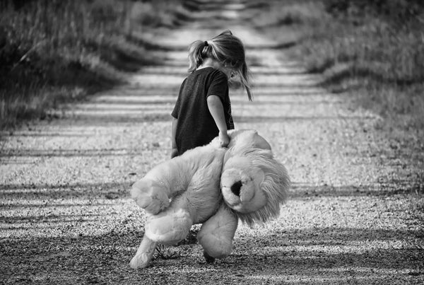 girl carrying a large stuffed lion down a dirt road