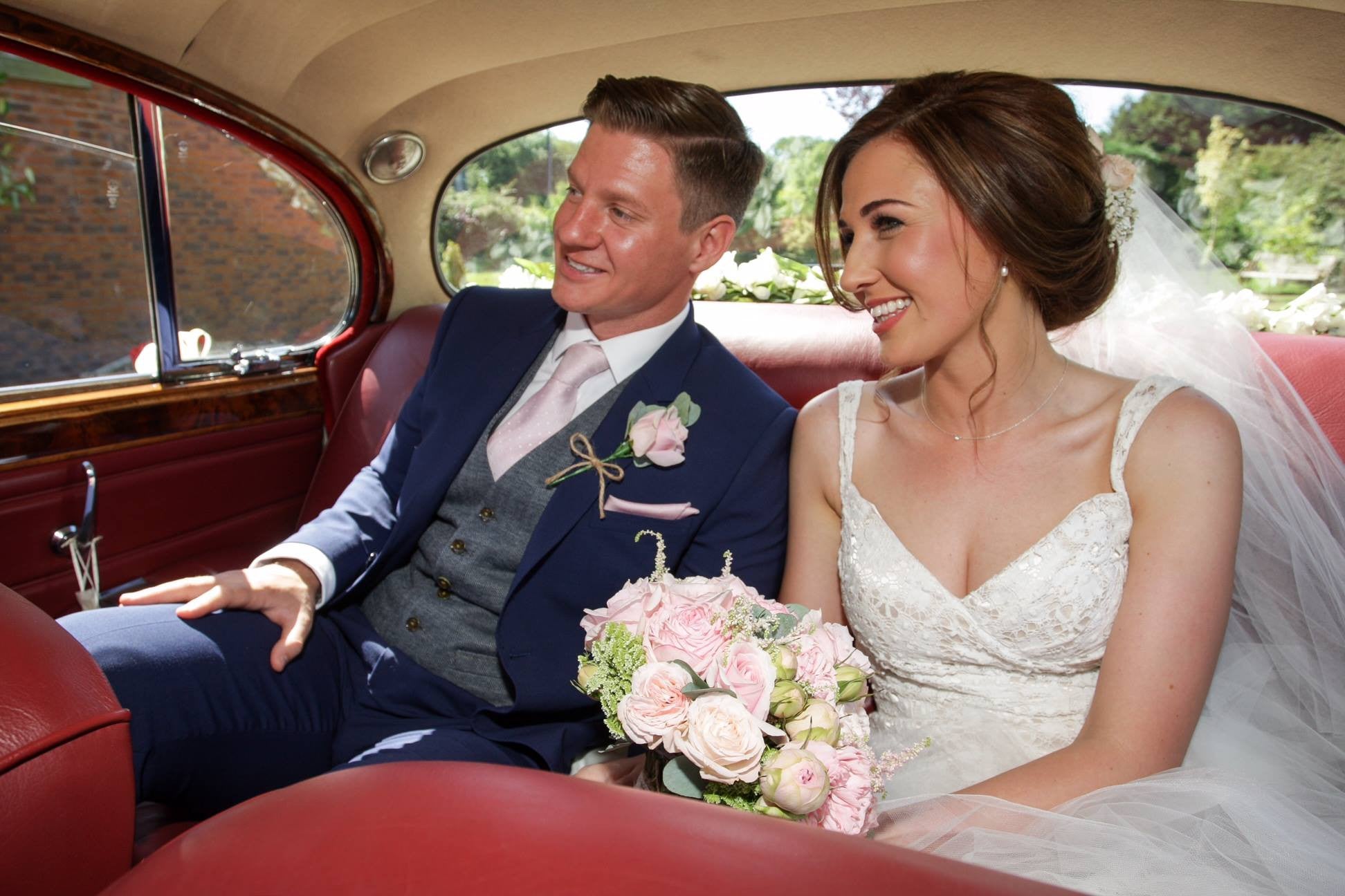 Bride and Groom in the wedding car with pink Rose bouquet and buttonhole.