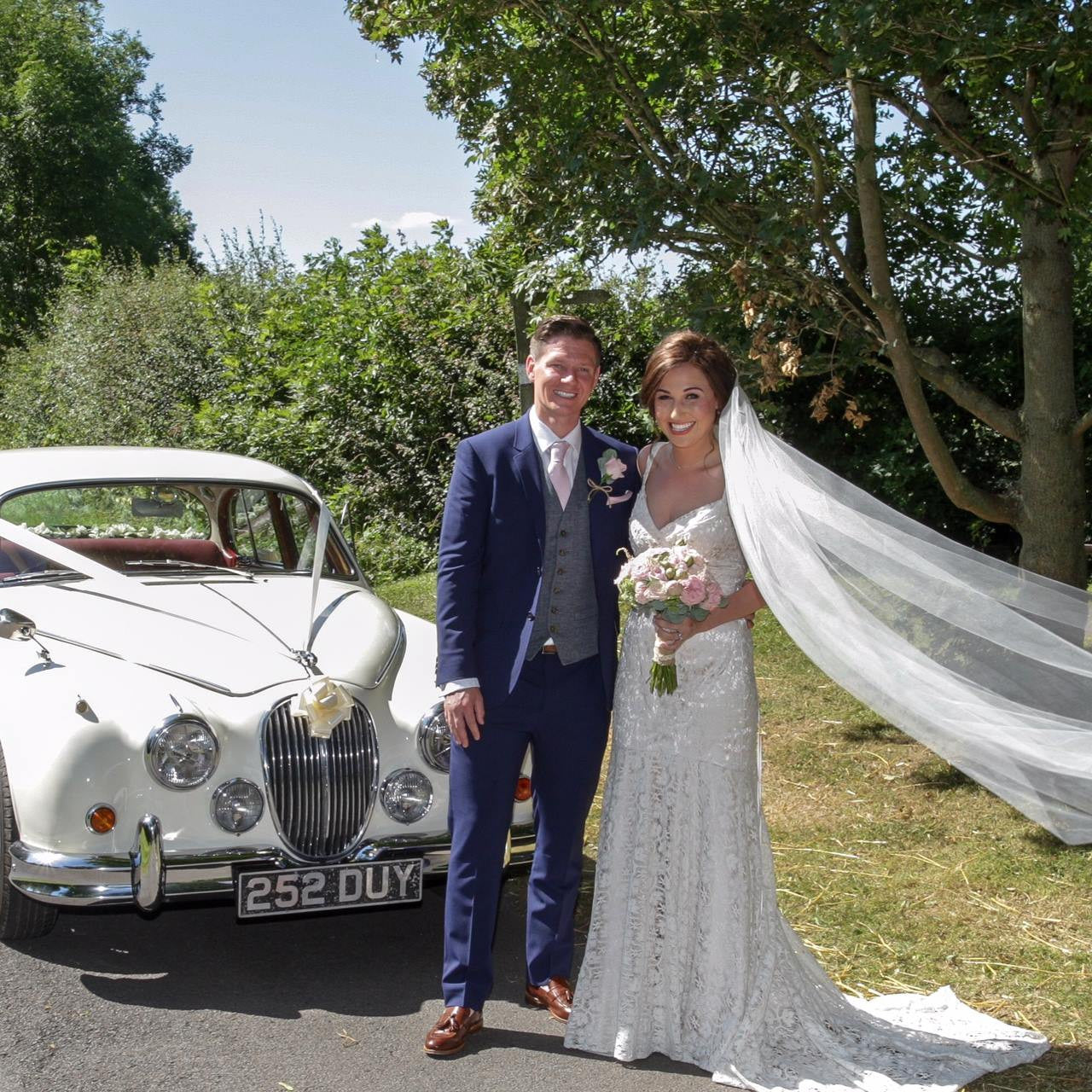 Bride and Groom with wedding car and wedding flowers.