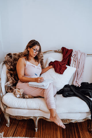 woman in lav and kush luxurious loungewear romper reaching a book on an armchair