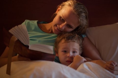 woman reading book to child in bed