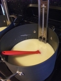 A red long handled spoon and cooking thermometer in a pan of fudge mixture 