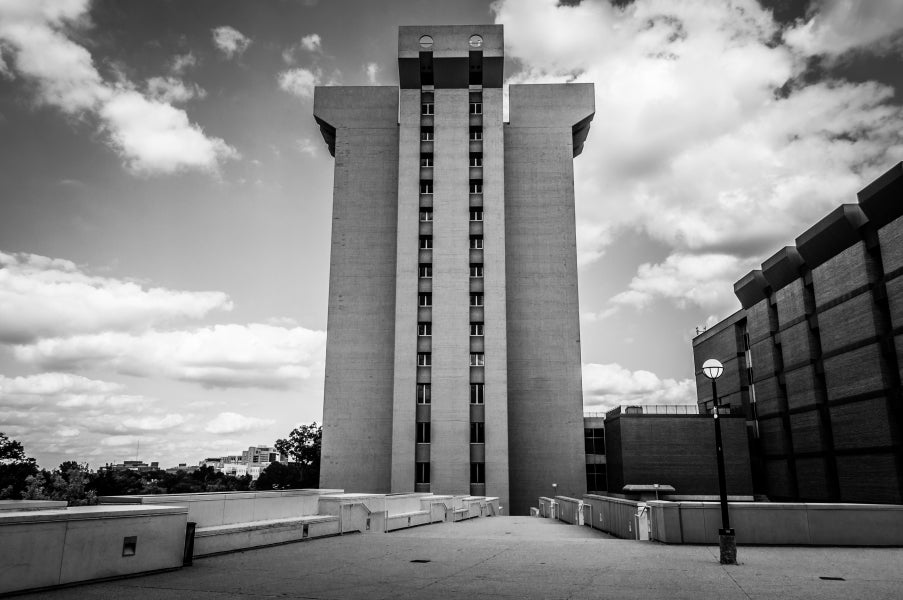 large building with a parking lot in front of it and clouds