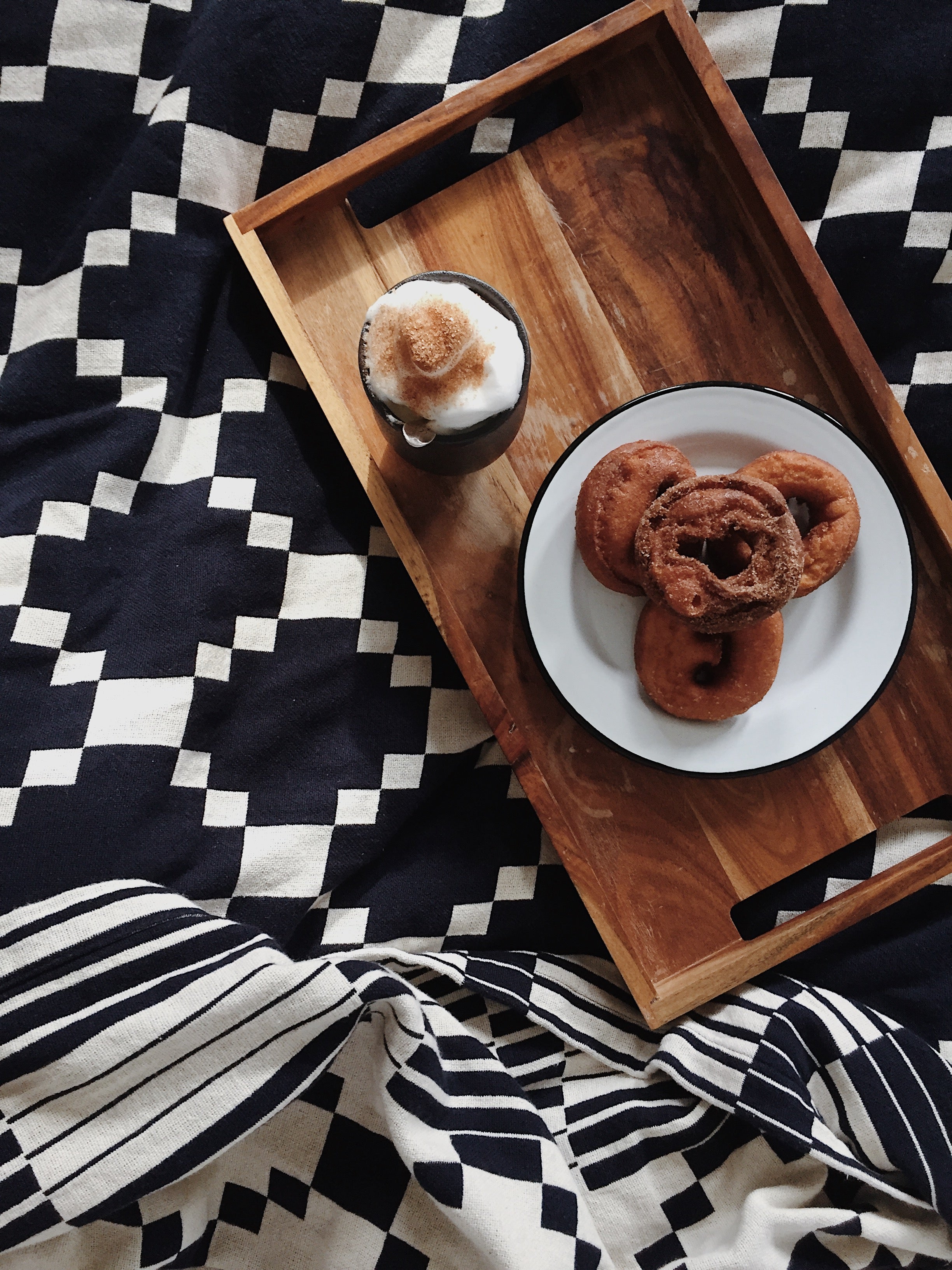 tray of coffee and pastries on a bed with black and white bedding