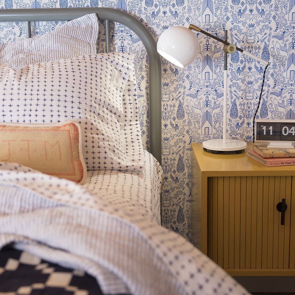 bed with patterned bed spread next to a wooden night stand and white lamp