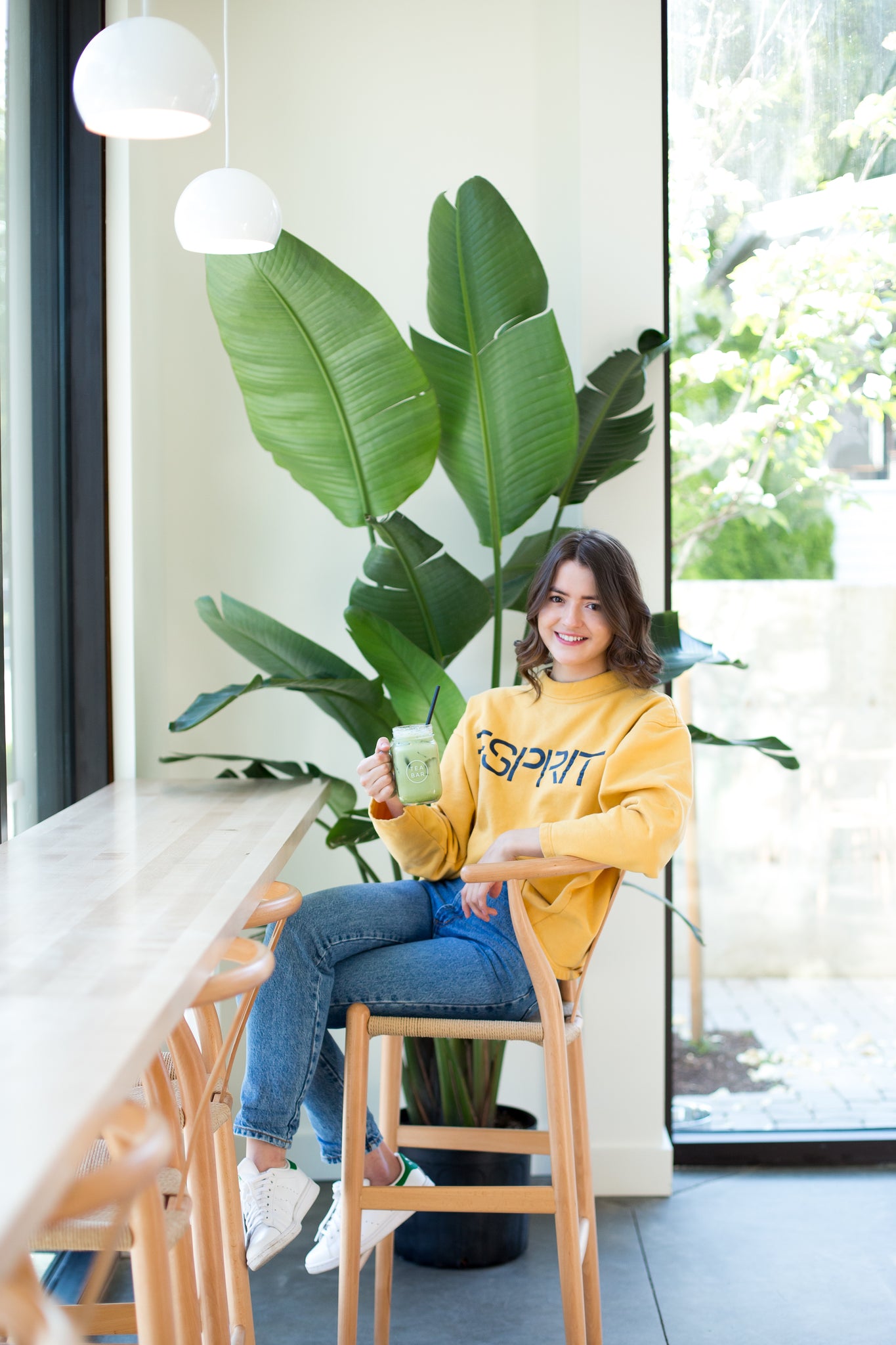 person sitting in a chair holding a drink in front of a large plant