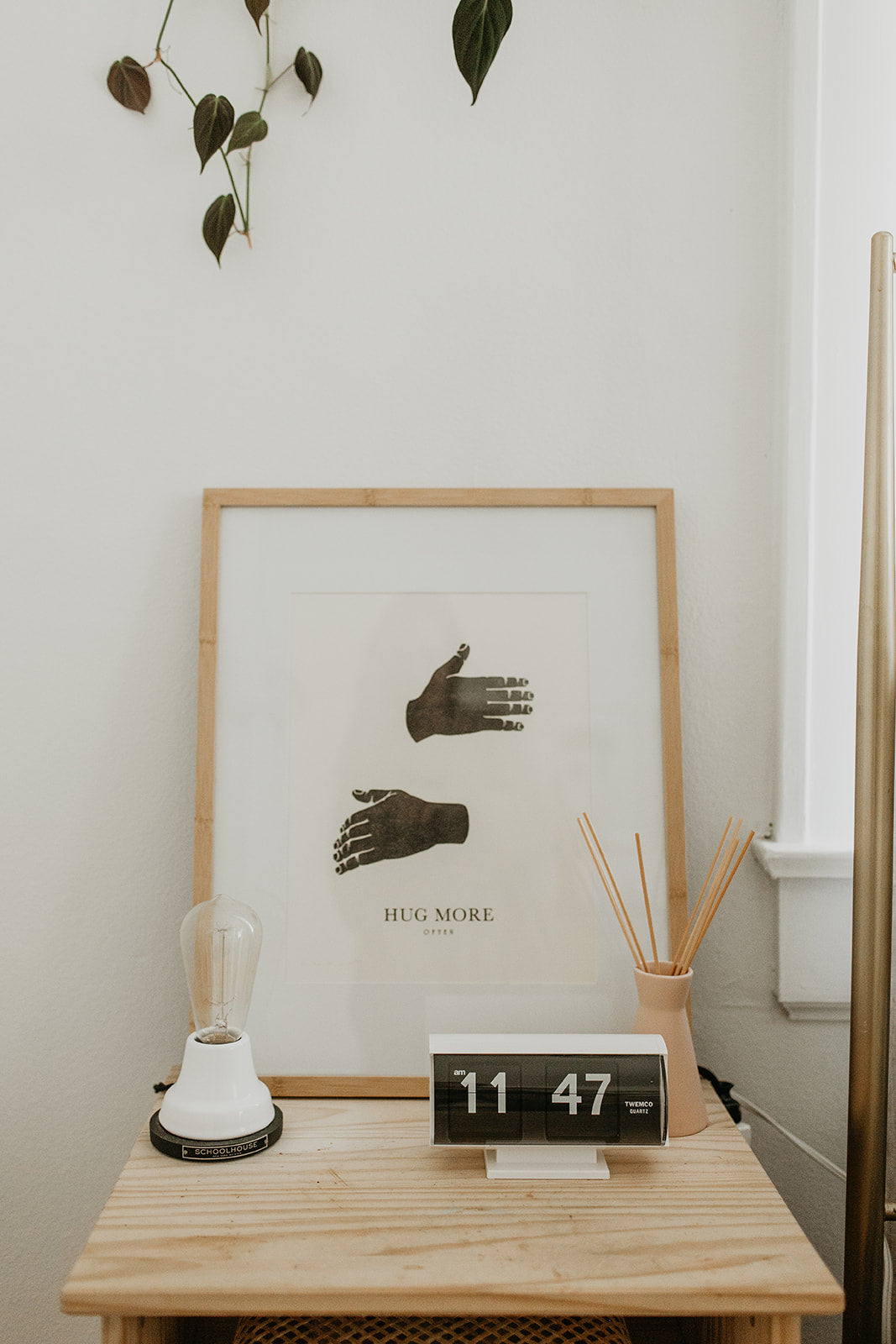 wooden nightstand with a white wall and a white framed piece of art and a black clock