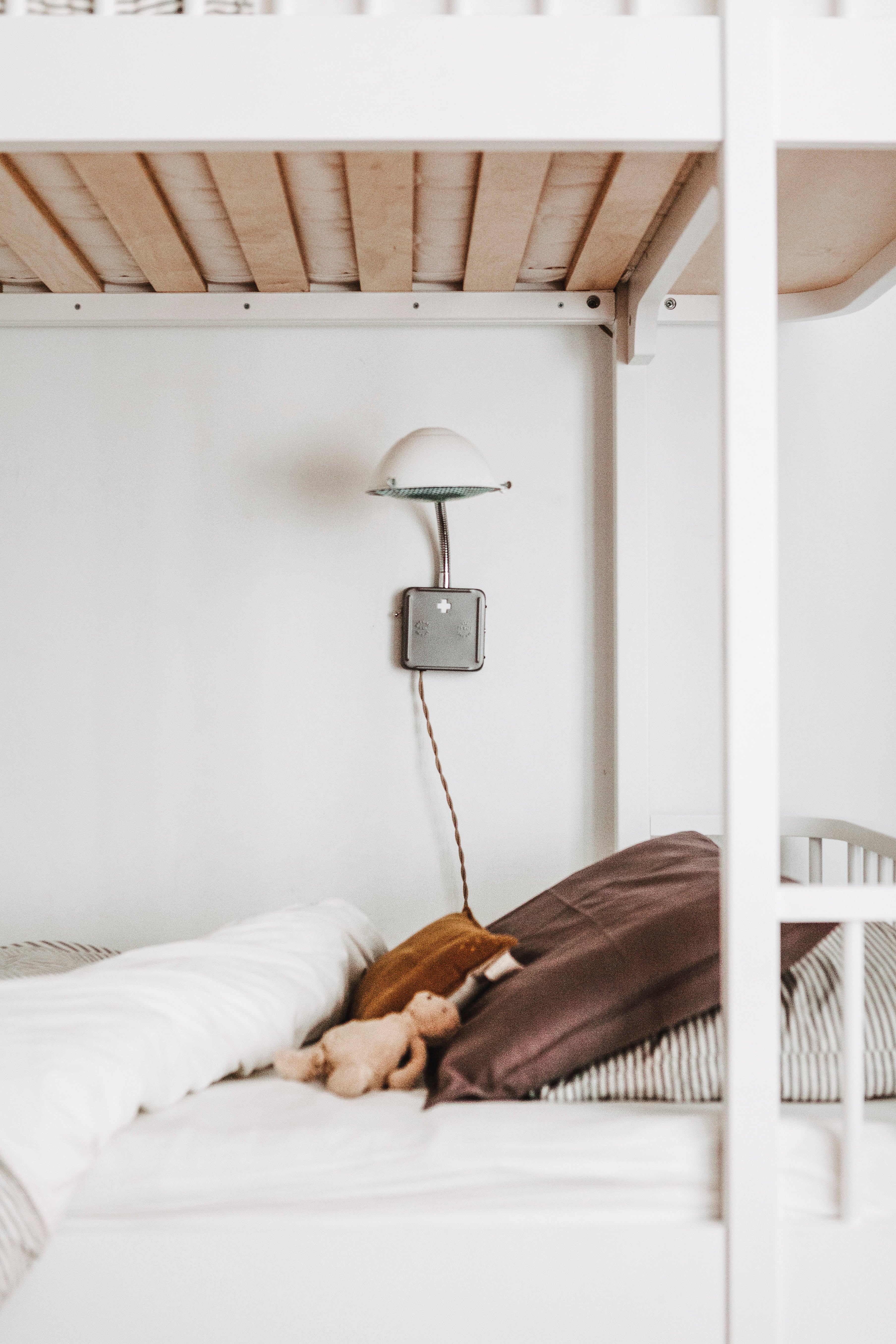 white sconce next to a bed with a brown pillow and white sheets