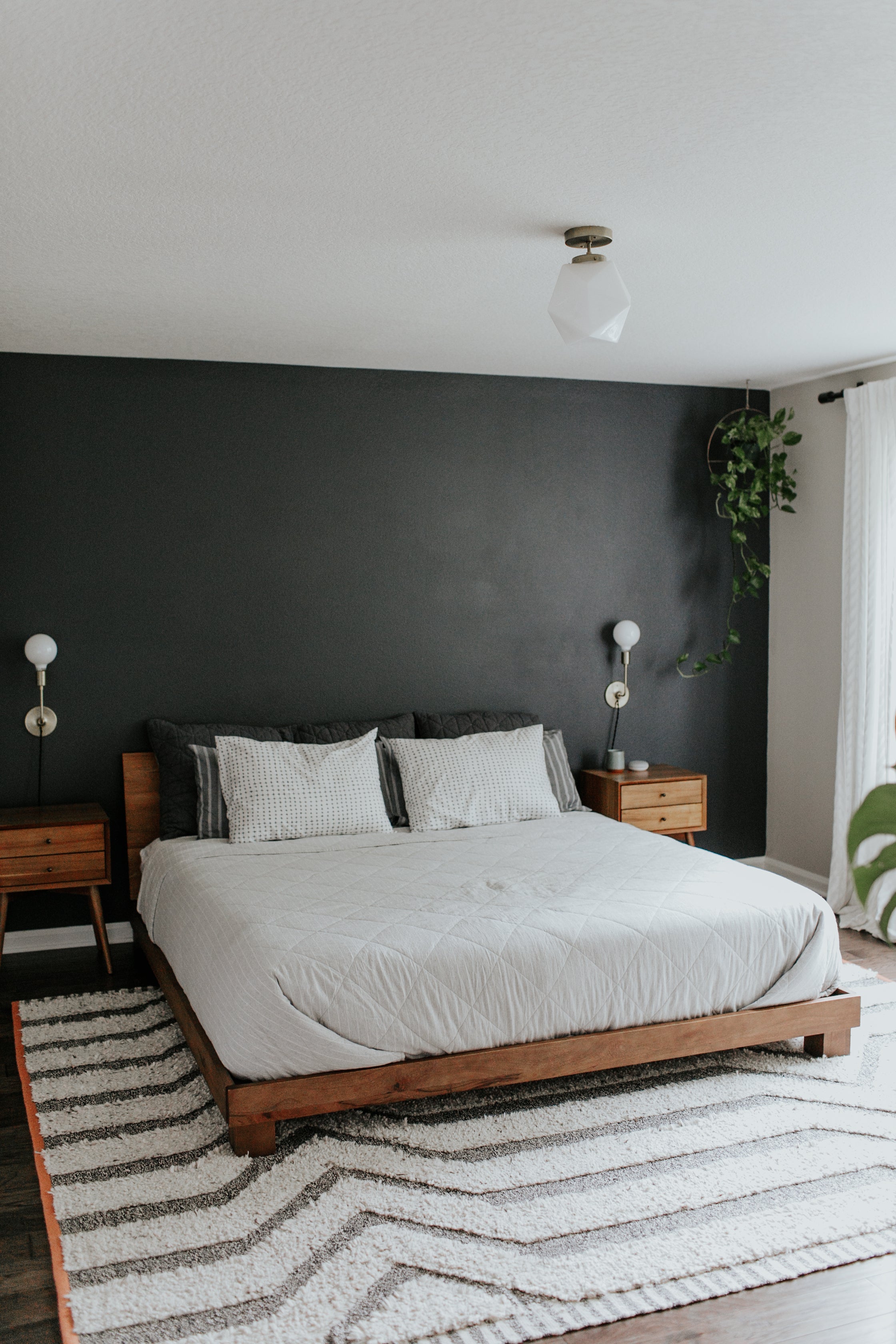 bed with a white comforter and a black accent wall and gray and white rug