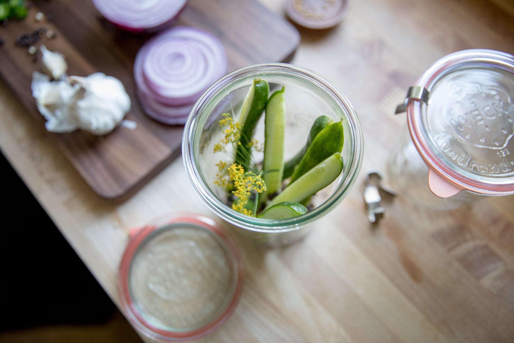 glass pickling jars with green vegetables next to sliced red onions 