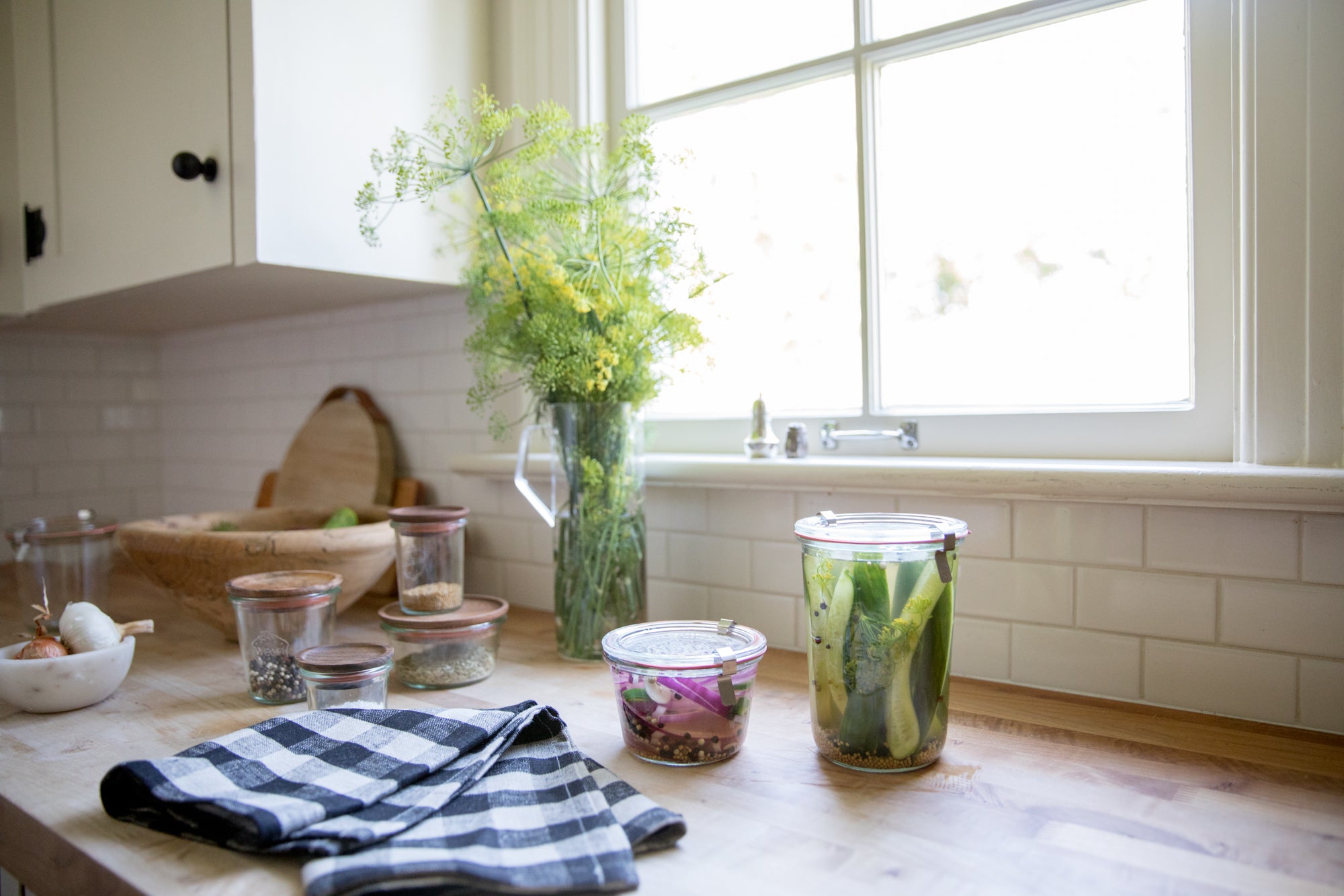 vase of flowers and jars of pickled vegetables on a kitchen counter