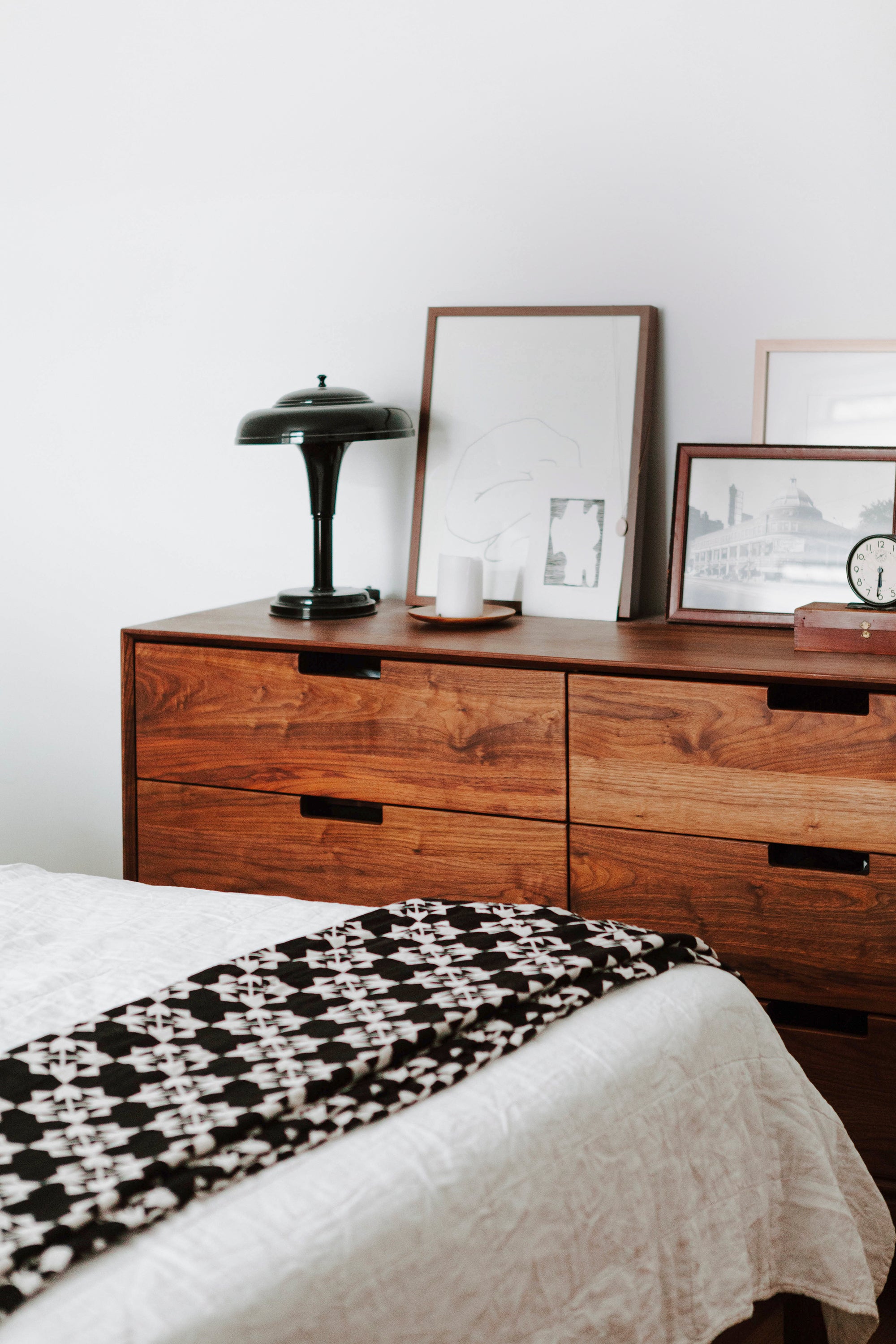 dresser with a lamp on it next to a bed with white sheets