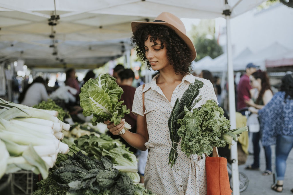 A young woman visits a farmers market to purchase fresh kale from a local farmer.