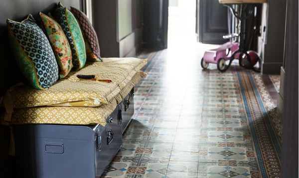 Patterned floor tiles in corridor with colourful cushions stacked on old suitcases