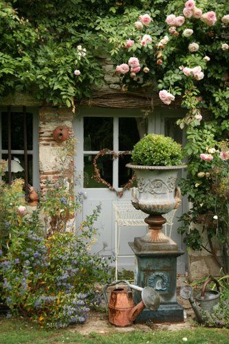 French copper watering can and medici urn on pedestal climbing rose rustic garden