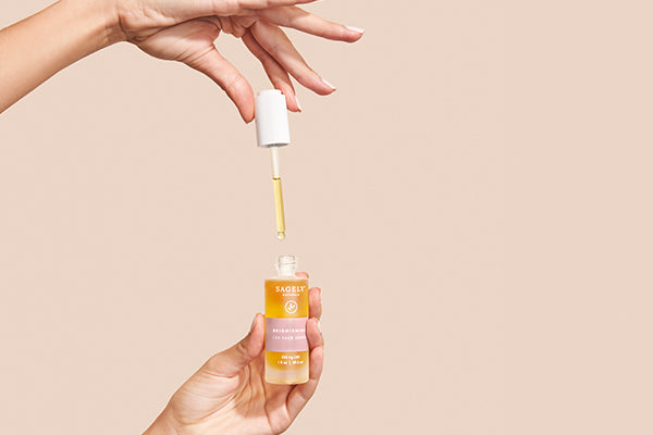 A hand squeezing the dropper of Sagely Naturals Brightening CBD Serum