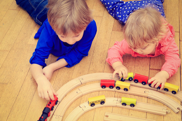 2 children playing with wooden trains