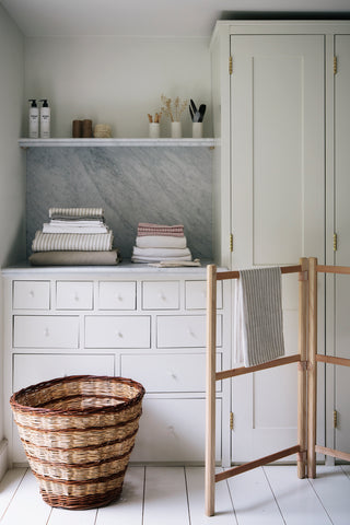 A wooden drying rack and a wicker basket in front of a white cupboard