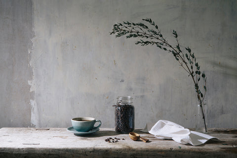 a blue coffee cup next to a wooden coffee scoop and a jar of coffee beans