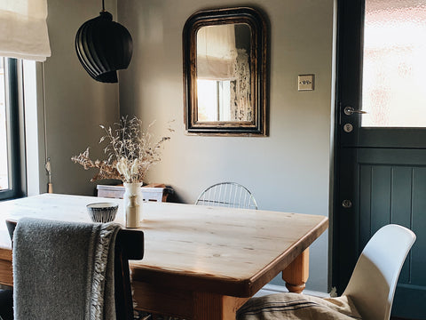 a wooden dining table in front of a dark door and antique mirror