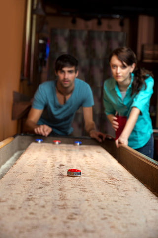 Two people testing shuffleboard pucks and trying to choose the best shuffleboard table.