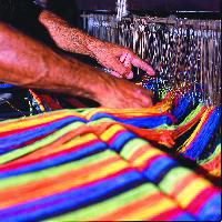 Hands knotting threads at weaving loom for hammocks