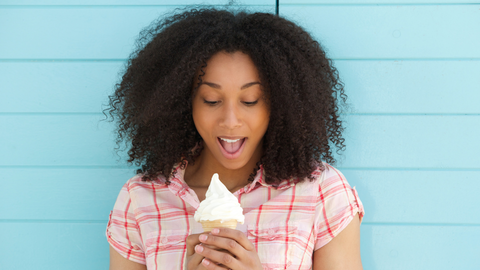 Black woman with curly hair looking down at melting ice cream