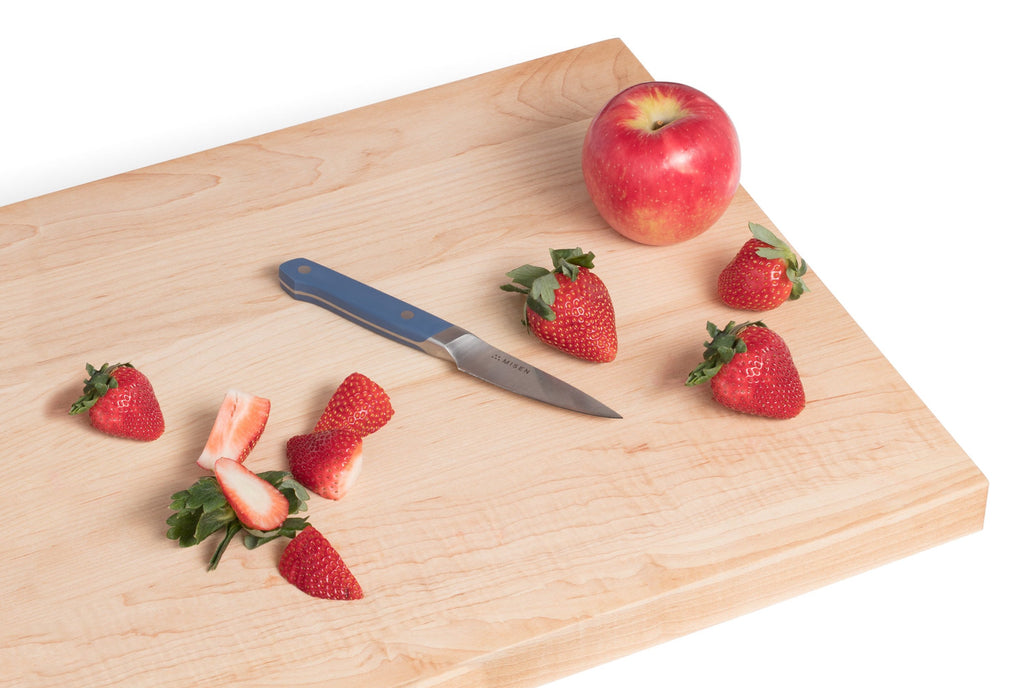A cutting board with fruit and a paring knife, one of the essential types of kitchen knives
