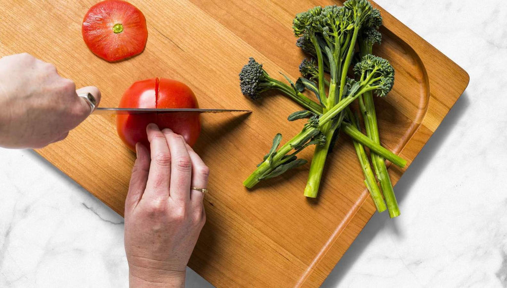 How to clean a wooden cutting board: A hand chops tomato on cutting board with rapini