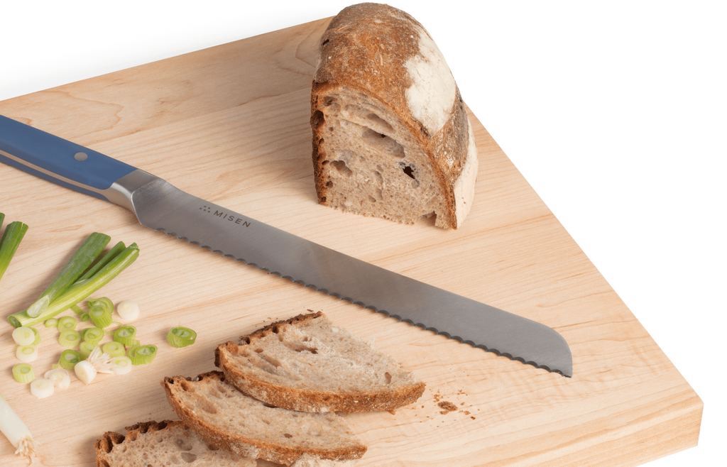A cutting board with sliced bread and a serrated knife, one of the essential types of kitchen knives