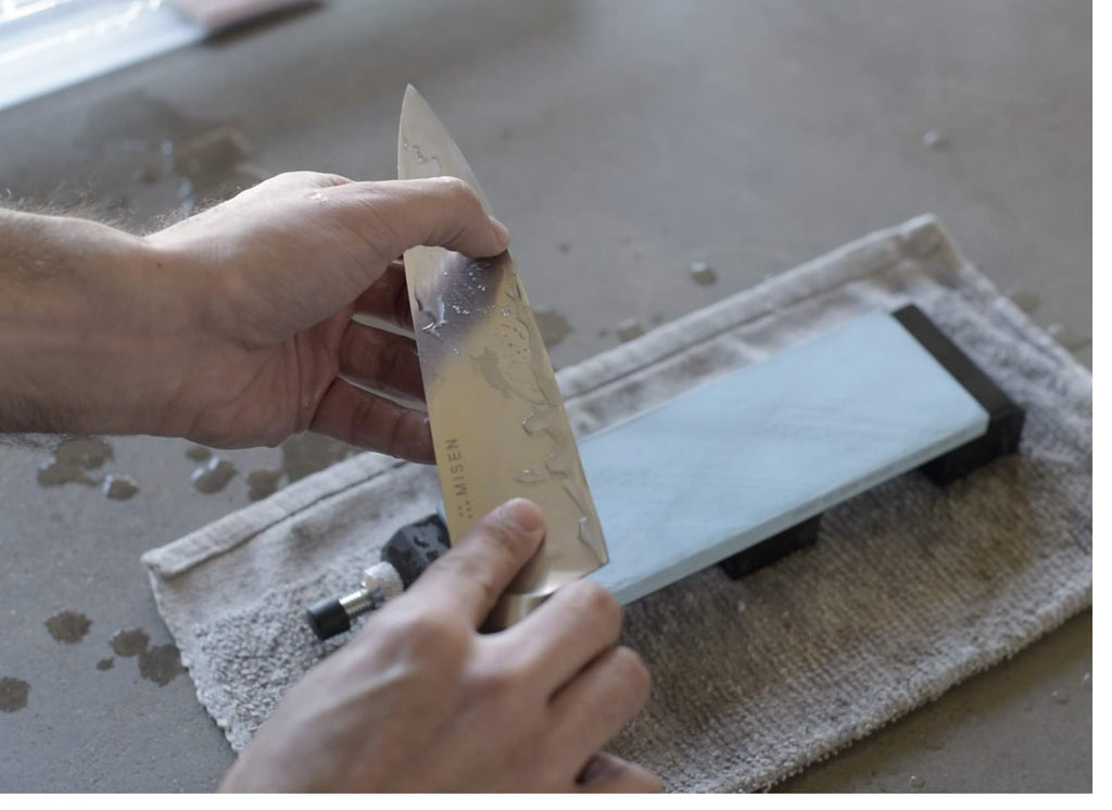 A man holds a knife above a Japanese water stone