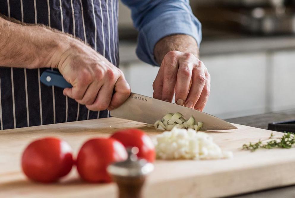 A home chops onions with a chef's knife, one of the essential types of kitchen knives