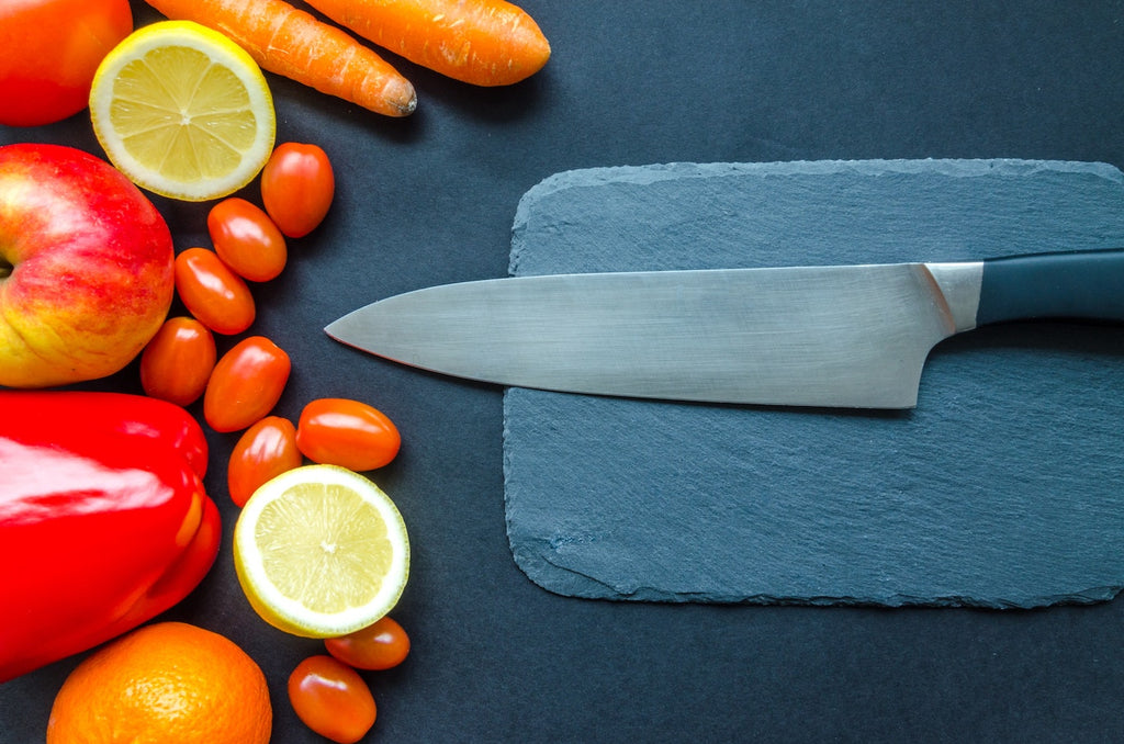 Knife tang: a chef's knife on a slate cutting board next to vegetables 