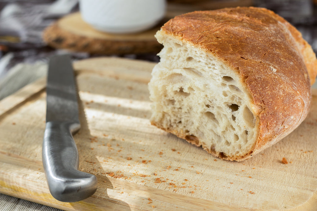 How to sharpen kitchen knives: a serrated knife on a cutting board next to a loaf of bread