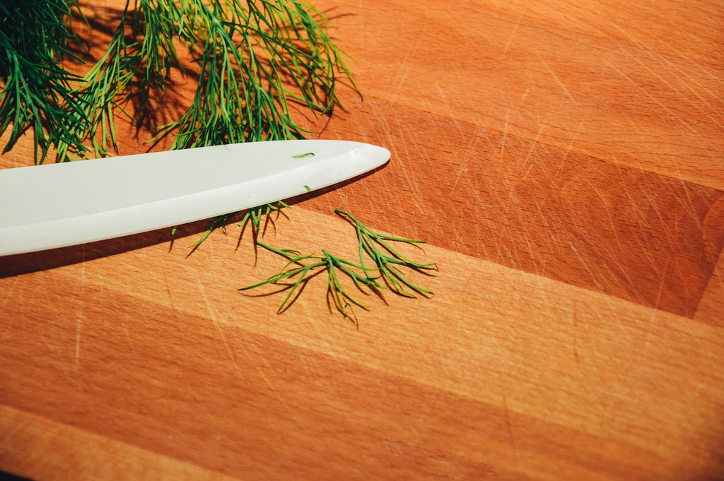 A knife blade and dill on a large cutting board