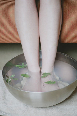 Two feet are in a stainless steel bowl filled with water and leaves
