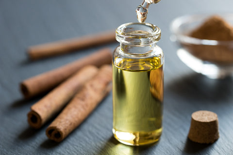 A glass bottle filled with yellow oil sits on a table next to cinnamon sticks